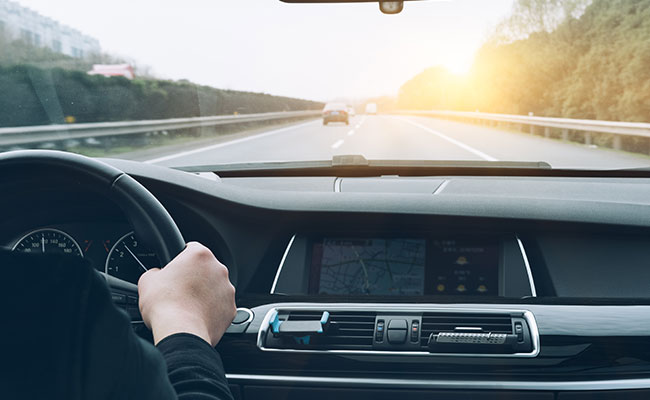 Driver's hands on a steering wheel on a highway at sunrise, view of the dashboard and navigation screen.