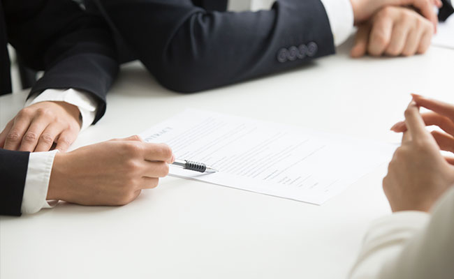 Business people reviewing a contract at a table, with one person pointing at the document using a pen.
