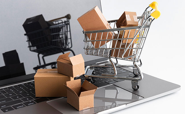 Miniature shopping cart filled with cardboard boxes placed on a laptop keyboard, symbolizing online shopping.