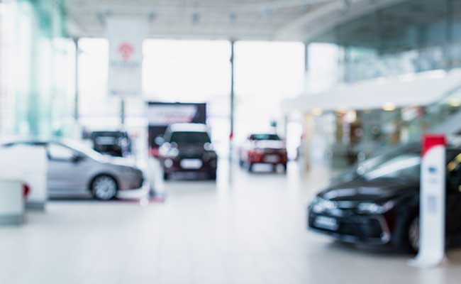 Interior view of a modern car dealership with multiple displayed vehicles in a bright, blurred setting