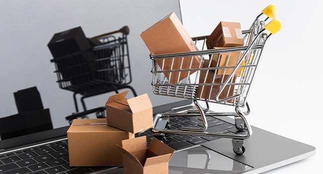 Shopping cart filled with cardboard boxes placed on a laptop keyboard, symbolizing online shopping and e-commerce.