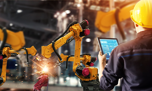 Engineer using a tablet to control robotic arms in a high-tech manufacturing facility.