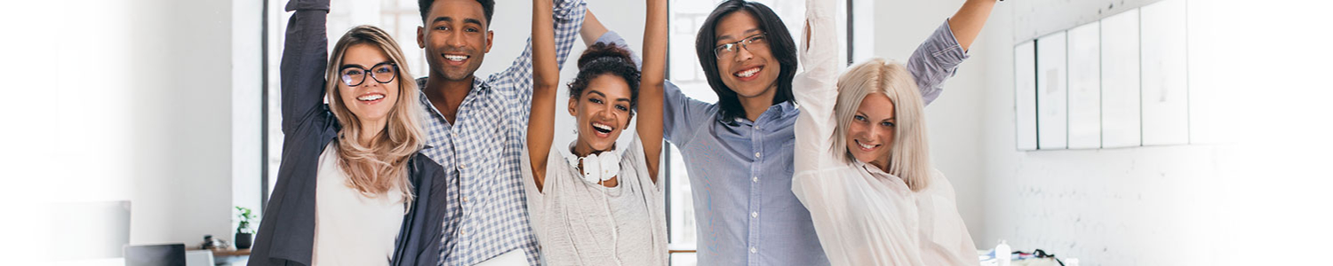 A group of happy and diverse young professionals standing together with raised arms, celebrating in an office environment.