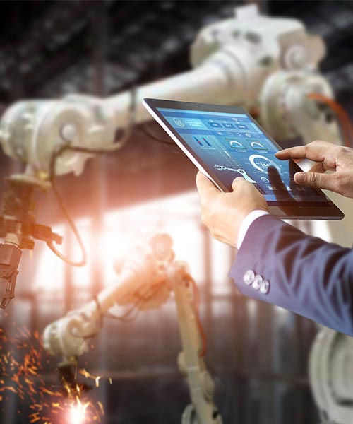 Business person using a tablet to control robotic arms in a smart factory environment.