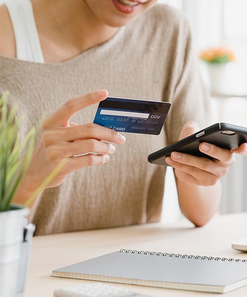 Woman using a credit card and smartphone for online payment at home.