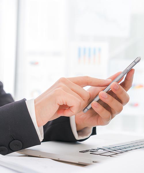 Businessperson using a smartphone in a modern office with charts in the background.
