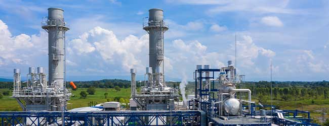 Moderne Industrieanlage mit Dampftürmen und Rohrsystemen in grüner Landschaft unter blauem Himmel – Symbol für Energieproduktion und industrielle Effizienz.