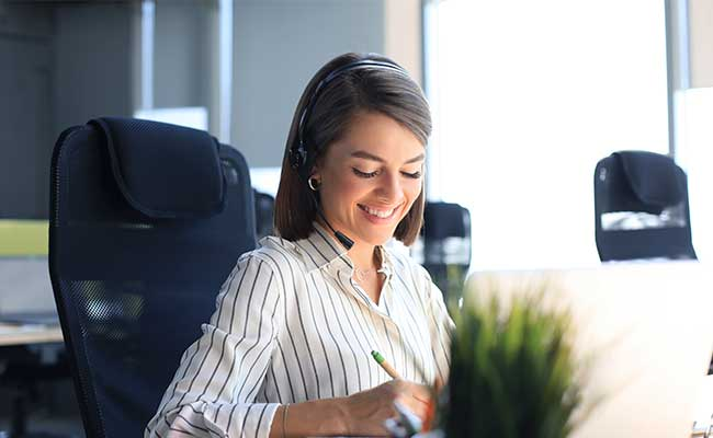 Freundliche Mitarbeiterin mit Headset im Gespräch am Schreibtisch.