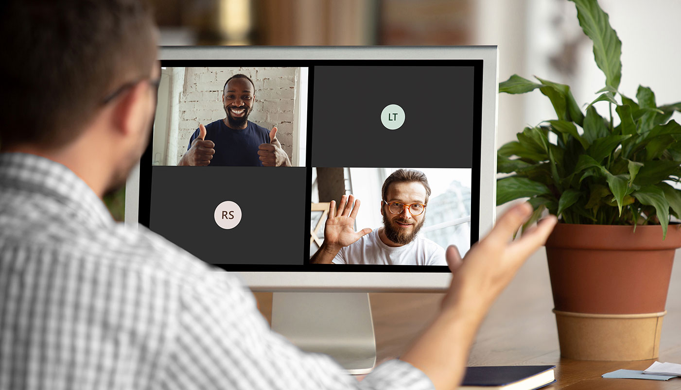 Ein Mann sitzt an einem Schreibtisch und führt ein virtuelles Meeting über Videokonferenz durch. Auf dem Bildschirm sind mehrere Teilnehmende zu sehen, die sich gegenseitig grüßen und lächeln. Die Szene veranschaulicht moderne digitale Zusammenarbeit und Kommunikation im Homeoffice als Teil des Digital Workplace.“